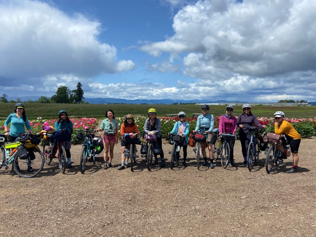 Ten riders pose with their bikes in front of flower plots.