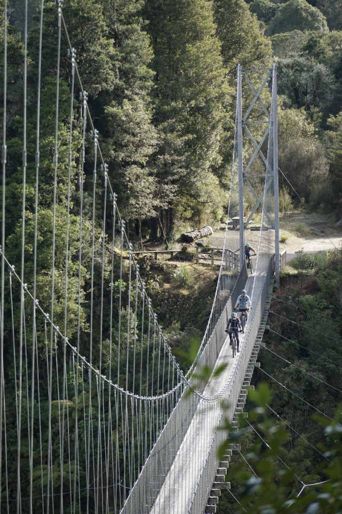 Three cyclists riding over a suspended bridge.