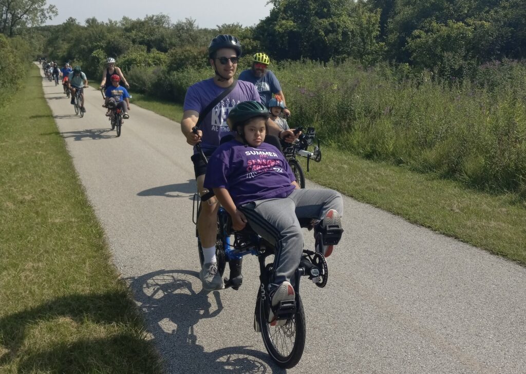 A cyclist pedals an adaptive bike with a passenger on the front using modified pedals