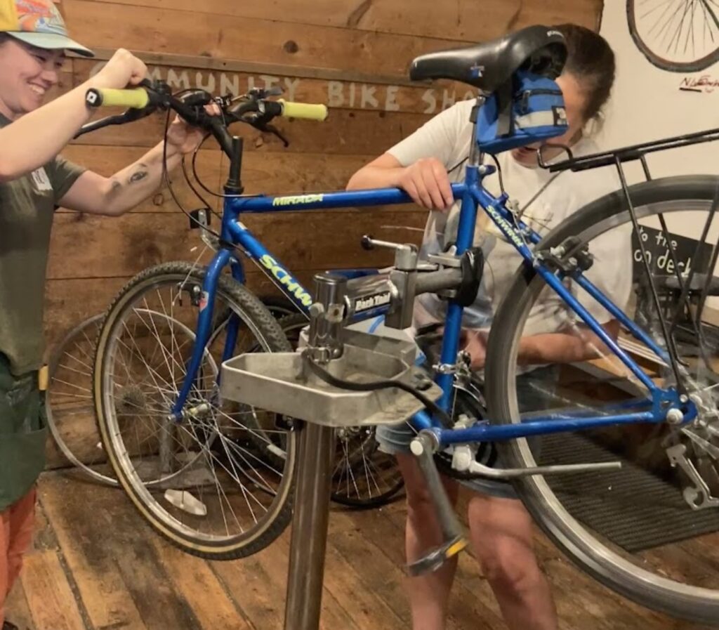 Two people work on bike maintenance with a bike on a bike stand