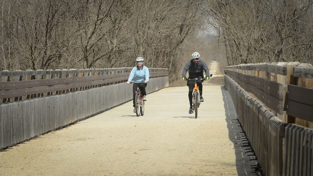 Two cyclists passing over a bridge at a time of year when there aren't any leaves.